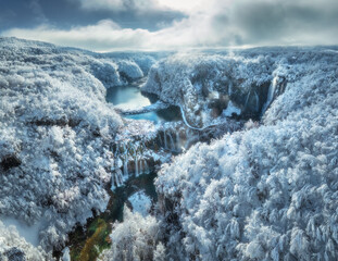 Wall Mural - aerial drone view of frozen lake, waterfall and snowy forest at sunset. winter fairytale in plitvice