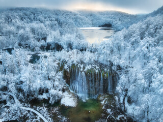 Wall Mural - aerial drone view of frozen lake, waterfall and snowy forest at sunset. winter fairytale in plitvice