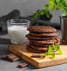 Wall Mural - Stack of chocolate cookies on a wooden board on a dark background with a glass of milk close up.