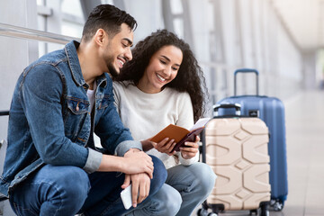 Wall Mural - Portrait Of Happy Young Arab Couple Waiting For Flight In Airport Terminal, Cheerful Middle Eastern Spouses Holding Passports And Tickets, Checking Departure Gate, Ready For Vacation Trip