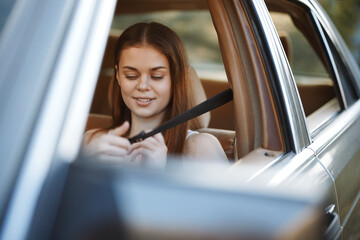 Poster - Young woman fastening her seatbelt inside a car, showcasing safety and comfort while enjoying a sunny drive, with a focus on her joyful expression and casual attire.