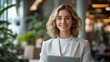 © somchai20162516 - Confident woman in business attire, smiling while holding a laptop in a modern office environment.