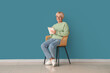 © Pixel-Shot - Old woman with notebook sitting on chair near blue wall