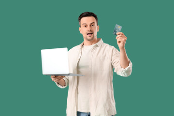 Wall Mural - Surprised man with laptop and credit card on green background