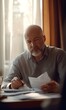 © Lucianastudio - Mature man wearing gray shirt reviewing documents while using pen at a desk by window