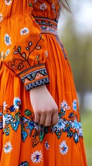 Woman wearing orange dress with floral embroidery detail.