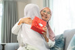 © Art_Photo - Muslim woman giving gift box to elderly mother, expressing love family bonding moment, happy holiday celebration, hijab women sharing joy, islamic cultural tradition, caring family relationship