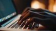 © Deni - Close-up of hands typing on a laptop keyboard in a dimly lit room.