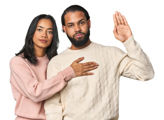 Wall Mural - Young Latino couple in studio taking an oath, putting hand on chest.