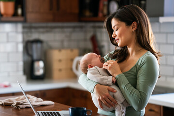 Wall Mural - Stay at home mom working remotely on laptop while taking care of her baby. Global work on computer