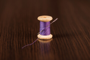 A sewing needle with a large eye is stuck into a spool of purple thread. Selective focus.