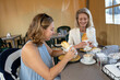 © Connect Images - Two women enjoying coffee and pastries at a cafe table, smiling and engaging in conversation, Netherlands