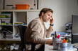 © Connect Images - Young man in a beige sweater works at a computer in a cluttered office, appearing thoughtful and focused while surrounded by books, Nijmegen, Netherlands