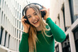 © Connect Images - Smiling woman in a green top enjoys music on her headphones in an urban setting, Berlin, Germany