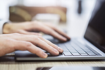 Wall Mural - With an office scene appearing softly blurred in the backdrop, the picture shows a close-up of male hands typing on a contemporary laptop keyboard