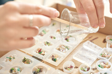 Hands pouring resin into molds for artistic jewelry making at craft workshop.