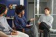 © Seventyfour - Portrait of African American woman as female therapist talking to teenagers sitting in circle during support group meeting in school copy space