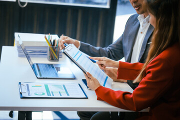 Wall Mural - A businessman and woman sit at a modern office table, smiling and discussing a new project or business startup. They collaborate with a laptop, focusing on strategic planning and teamwork