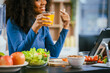 © NanSan - African American woman sitting  table, enjoying a colorful salad orange juice, highlighting the health benefits of five-color fruits vegetables, rich in antioxidants, reducing cancer risks,wellness