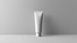 © Andrey - A minimalist white cosmetic tube mockup is placed upright against a smooth grey background, showcasing a sleek and modern packaging design for beauty products.