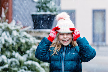 Wall Mural - Funny portrait of little school girl in winter clothes. Happy positive child outdoors. Winter day, snow falling. Cold weather and snowing.