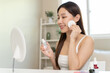 © Pormezz - Happy asian woman looking at mirror and using cotton pad clean make up on her face