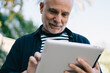 © BullRun - Cheerful aged man browsing tablet in city park