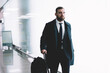 © BullRun - Confident businessman with suitcase walking along airport corridor