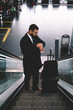 © BullRun - Caucasian businessman checking time on modern smartwatch hurry up to airport gate in terminal, formally dressed commuter with luggage suitcase standing on electronic escalator during work travelling