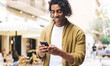 © BullRun - Smiling handsome 20s male blogger share media content via mobile phone walking on city street, happy hipster guy millennial strolling and reading test message notification on smartphone in city