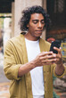 © BullRun - Positive young male in casual trendy wear using navigation app walking on city street during travel journey, smiling hipster guy influencer holding smartphone sending content share multimedia online