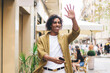 © BullRun - Positive ethnic man with smartphone waving hand on street