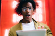 © BullRun - Expressive young curly male in eyewear holding digital tablet connected to 20s shocked with news from social media, stressed man blogger feeling anger about messages getting on touchpad outdoors