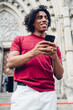 © BullRun - Happy young ethnic tourist guy chatting on smartphone near entrance of cathedral