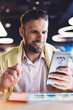 © BullRun - Cheerful male user connecting to coworking wireless internet for browsing website via smartphone gadget, happy smiling man writing mobility mail during cellphone messaging and content texting