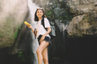© BullRun - Young female traveler standing near waterfall with cellphone