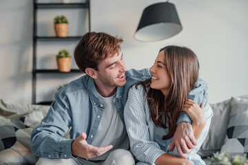 Wall Mural - Head shot positive loving bonding married couple sitting on comfortable sofa, looking at camera, holding video call with friends. Happy family bloggers recording video for personal channel at home..