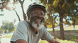 © DEIB Visuals - A smiling senior black man riding his moutain bicycle along a tree-lined path in a park, Happy elderly african man cycling on bike to keep fit healthy & active