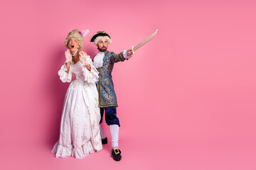 Elegant couple in vintage costumes posing with dramatic expressions on a pink background