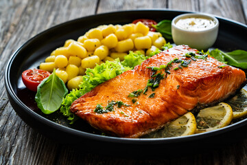 Wall Mural - Seared salmon steak with gnocchi and lemon slices served on black plate on wooden table	