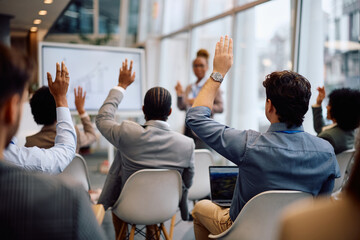 Rear view of a business people raising their hands hand to ask question during seminar in conference room.