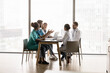 © fizkes - Five multi-ethnic medical workers take part in scheduled meeting in modern clinic conference room, sit at table and lead talk, share opinions, professional vision and skills. Collaboration, medicine