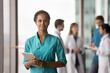 © fizkes - Portrait of pretty African woman doctor wearing turquoise scrub uniform posing in modern clinic office, looking at camera, holding digital tablet, colleagues blurred in background. Mission, healthcare