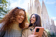 © CarlosBarquero - Young only women friend using mobile phone in hands in front of Sagrada Familia in Barcelona. Beautiful caucasian girls at European city enjoying vacation happy and smiling. Funny tourism smile people