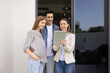 © fizkes - Positive professional realtor woman meeting with young couple of renters at apartment, using tablet, showing screen to customers, standing on rental doorstep, talking , laughing