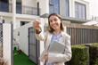 © fizkes - Happy real estate professional agent woman offering key from new home, standing at house, apartment, townhouse for sale or rent, looking at camera, smiling, posing for work portrait