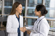 © fizkes - Women colleagues, hospital staff members having friendly informal talk standing in clinic office, greeting, shake hands, express respect, finish medical concilium meeting successfully, reach agreement