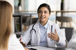 © fizkes - Young Indian female general practitioner wear white lab coat make speech, female patient listening health advice, get professional care, comprehensive treatment option, test results at visit in clinic