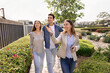 © fizkes - Happy professional realtor woman giving tour around well suburb neighborhood for house buyers, showing apartment exterior, location to young couple of customers, walking outside, pointing hand away