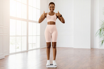excited sporty woman standing on scales at home or fitness studio, happy with result of her diet and